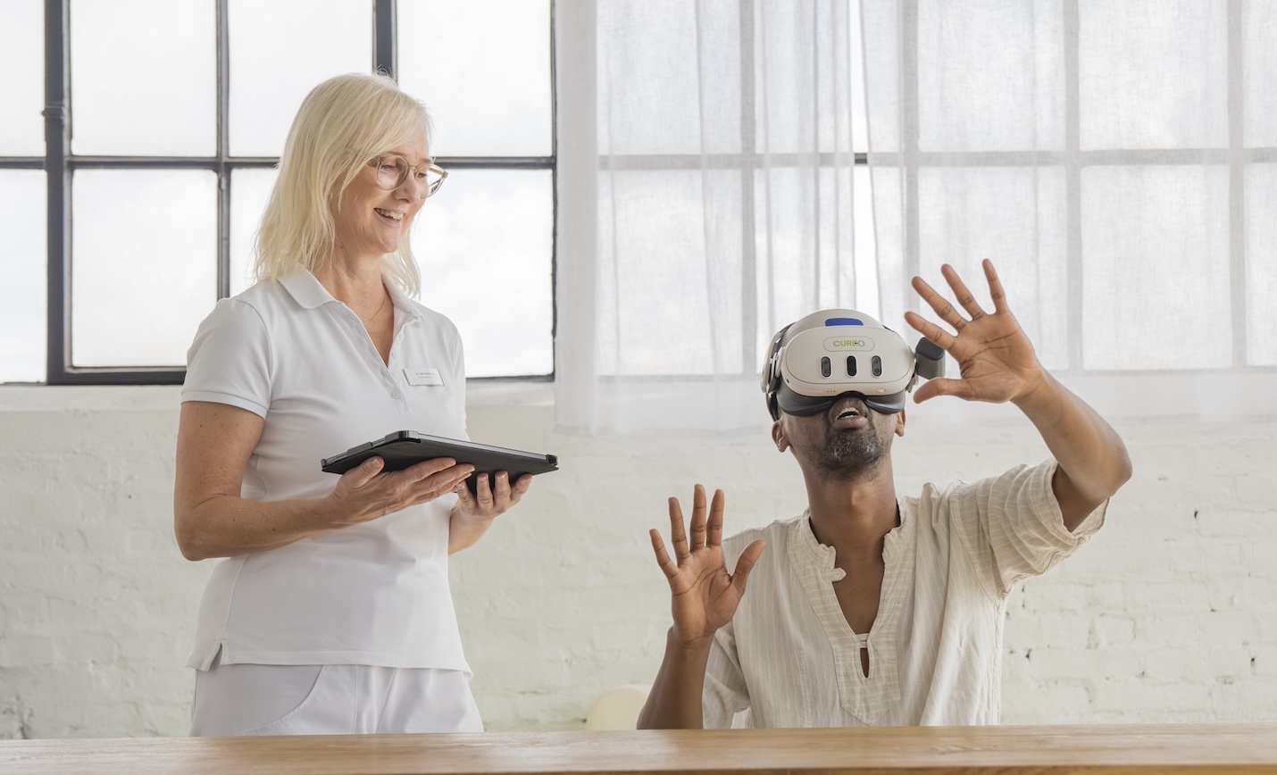 Therapeutin steuert über ein Tablet eine VR-Therapiesitzung mit CUREO, während eine Patientin die VR-Brille trägt und mit den Händen interagiert
